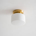 Straight-on view of this Clérachic flush-mount light, switched off, with the white glass drum shade and brushed brass canopy on a grey ceiling.