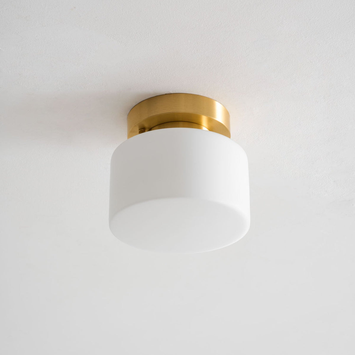 Straight-on view of this Clérachic flush-mount light, switched off, with the white glass drum shade and brushed brass canopy on a grey ceiling.
