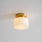 A Clérachic flush-mount light lit warmly, the frosted white shade glowing softly against a grey ceiling with a brass canopy above.