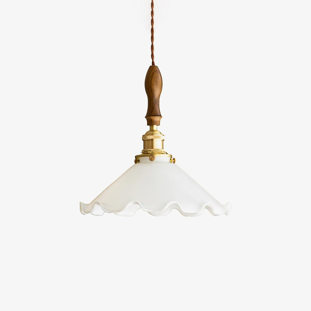 A Clérachic pendant light on a plain white backdrop, a ruffled white glass shade under a walnut handle and brass fitting on a twisted cord.