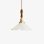 A Clérachic pendant light on a plain white backdrop, a ruffled white glass shade under a walnut handle and brass fitting on a twisted cord.