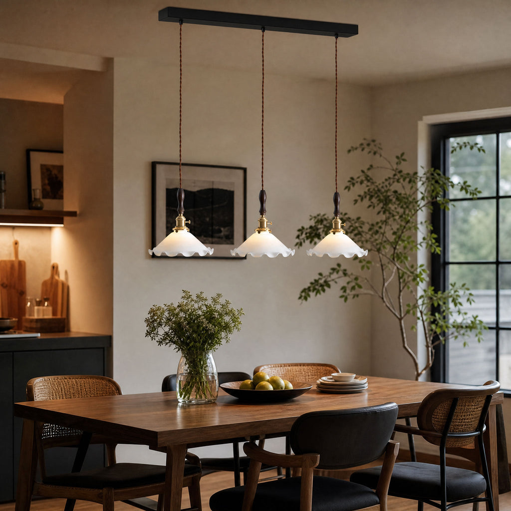 A row of three ruffled glass shades from this Clérachic pendant light hangs above a timber dining table with black cane chairs.