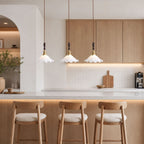 Three ruffled shades from this Clérachic pendant light hang above a pale breakfast bar with oak stools and an oak cabinet wall.