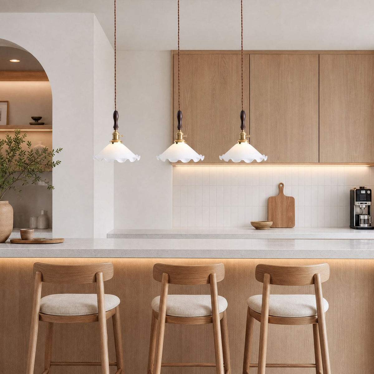 Three ruffled shades from this Clérachic pendant light hang above a pale breakfast bar with oak stools and an oak cabinet wall.