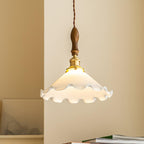 Close view of the ruffled white shade, walnut handle and brass fitting of this Clérachic pendant light against a warm yellow wall.