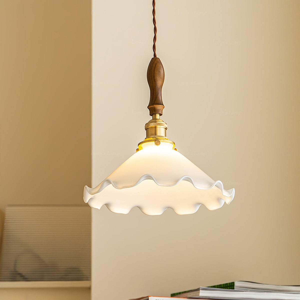 Close view of the ruffled white shade, walnut handle and brass fitting of this Clérachic pendant light against a warm yellow wall.