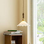 This Clérachic pendant light hangs beside a blinded window above a small wooden side table stacked with books.