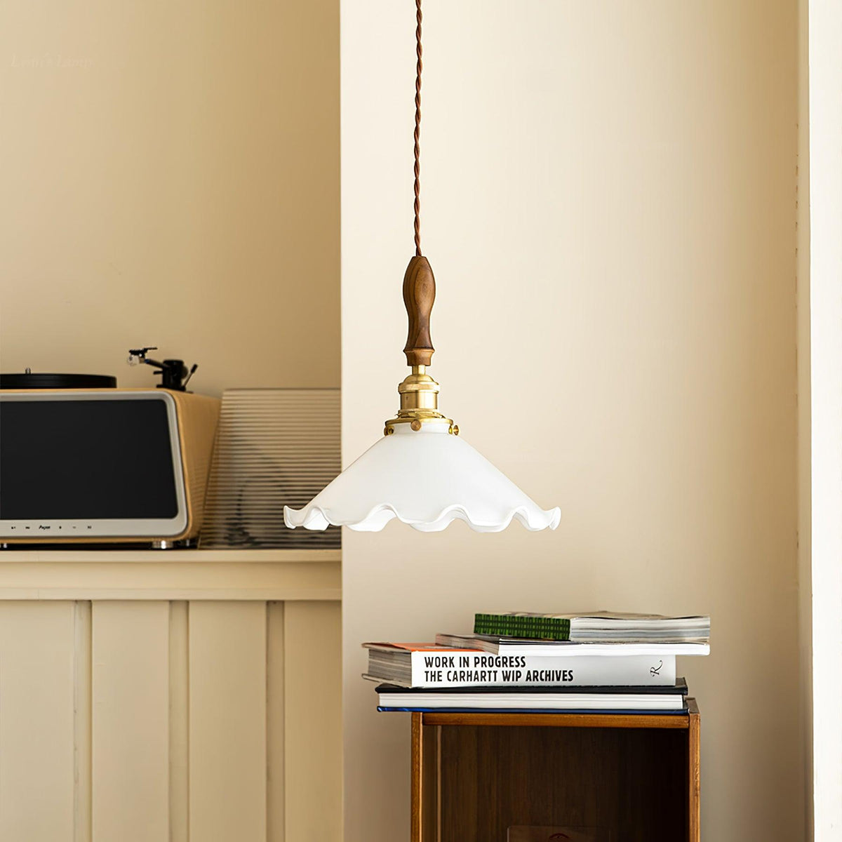 A Clérachic pendant light hangs in a cream corner above a stack of books, with a retro radio on a shelf behind.