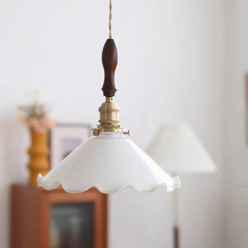 Close, soft-focus view of this Clérachic pendant light, its brass switch socket and walnut handle above the white glass shade.