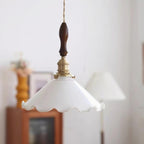 Close, soft-focus view of this Clérachic pendant light, its brass switch socket and walnut handle above the white glass shade.