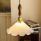 Warm light fills the ruffled shade of this Clérachic pendant light, hung above magazines and a wooden shelf.