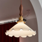 Looking up at this Clérachic pendant light, a wavy-edged white shade lit from within against an arched wall and a red curtain.