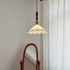 This Clérachic pendant light hangs in the upper part of the frame against a grey wall, beside white curtains and a mirror frame.