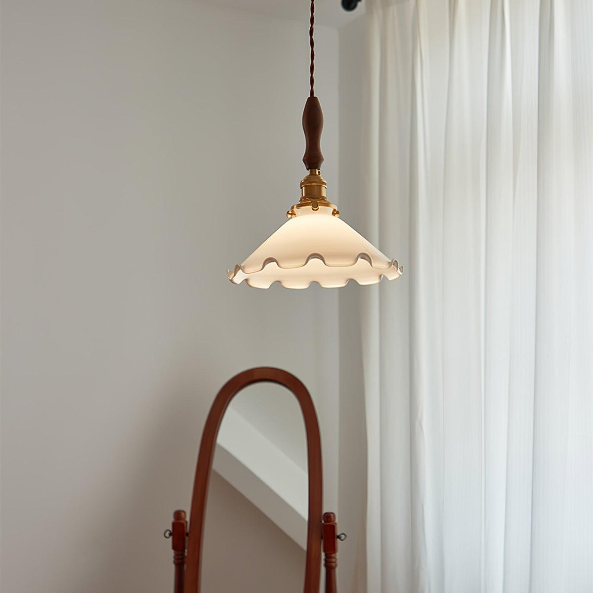 This Clérachic pendant light hangs in the upper part of the frame against a grey wall, beside white curtains and a mirror frame.