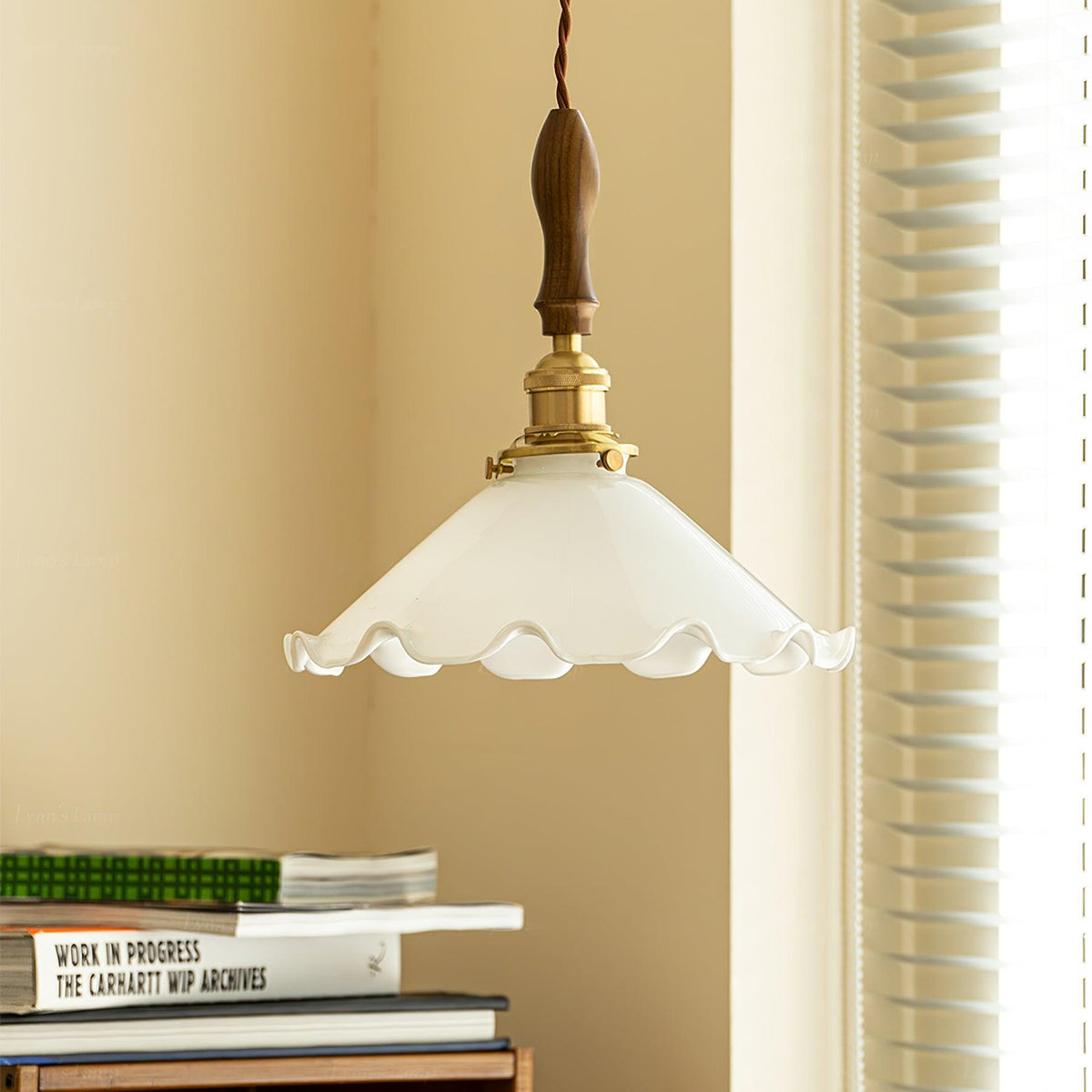 This Clérachic pendant light hangs beside a sunlit window with blinds, above a pile of books on a shelf.