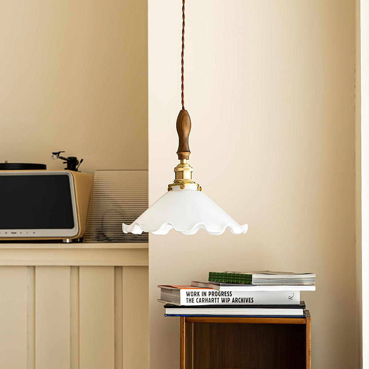 A Clérachic pendant light hangs in a warm cream corner above a retro radio and a stack of books.