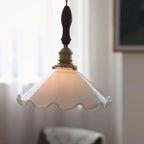 Softly lit, this Clérachic pendant light glows in front of sheer white curtains with a faint armchair visible behind.