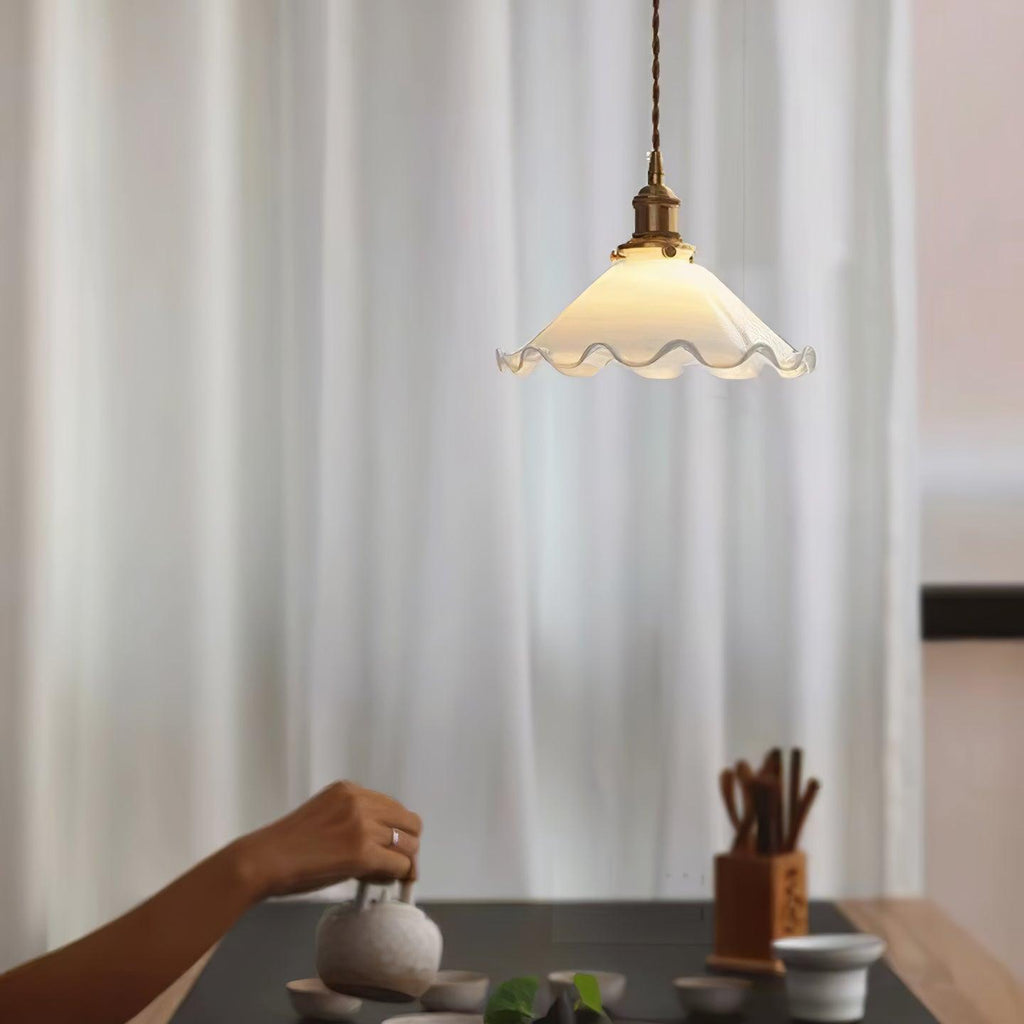 A Clérachic pendant light hangs beside sheer white curtains above a tea tray and hands pouring from a teapot.