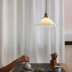 A Clérachic pendant light hangs beside sheer white curtains above a tea tray and hands pouring from a teapot.