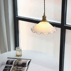 This Clérachic pendant light hangs beside a black-framed window above a round white table with an open book and a glass.