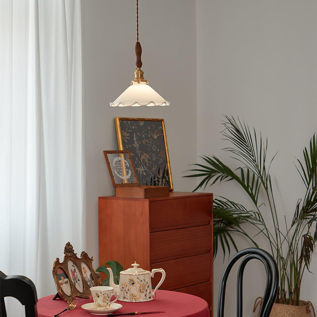 A small Clérachic pendant light hangs high above a red-clothed table set with a teapot, with a teak chest and palm behind.