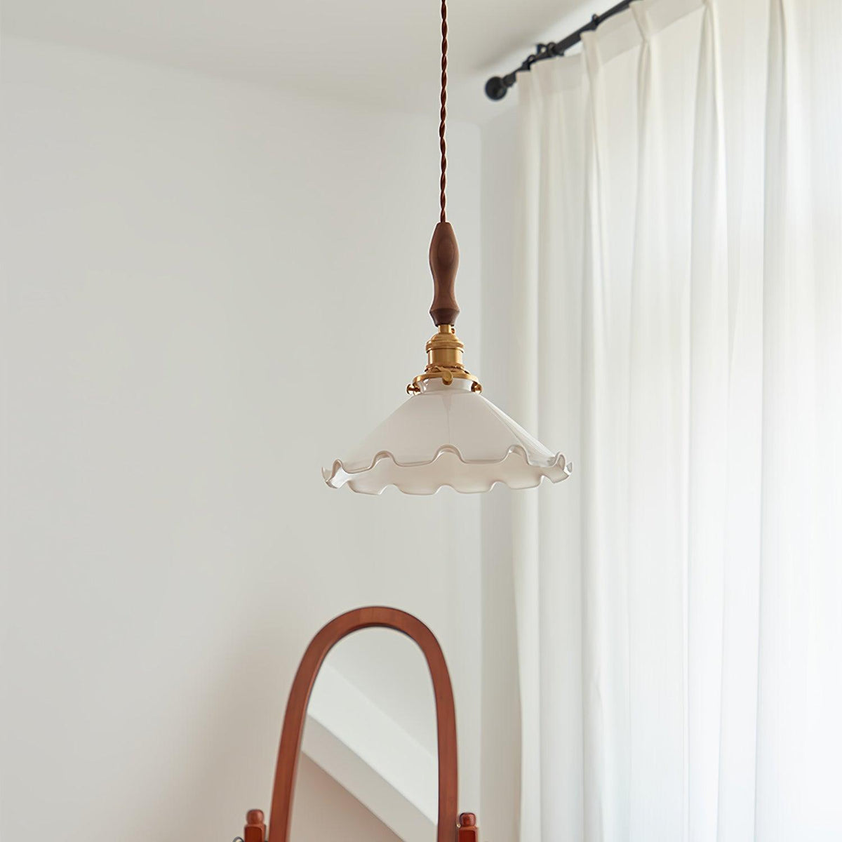 Against a white wall with a curtain rail, this Clérachic pendant light hangs above the arch of a wooden mirror frame.