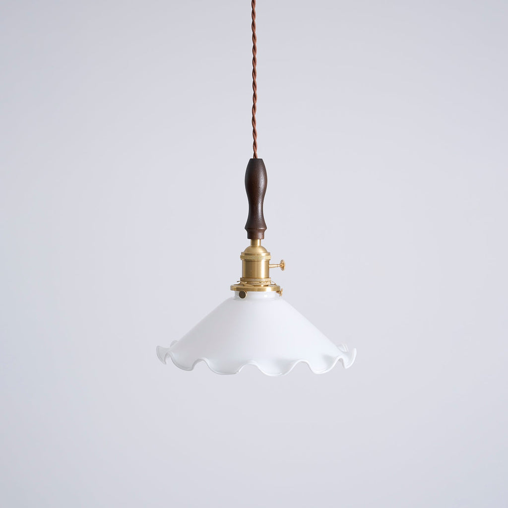 This Clérachic pendant light on a plain pale grey backdrop, with a brass socket and a dark walnut handle above a white shade.