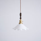 This Clérachic pendant light on a plain pale grey backdrop, with a brass socket and a dark walnut handle above a white shade.