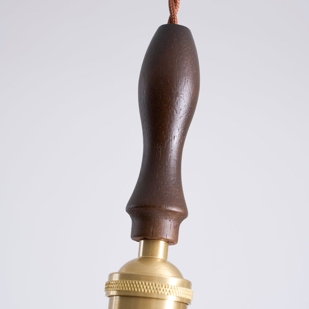 Close view of the dark walnut handle and brass fitting of this Clérachic pendant light, with the cord entering at the top.