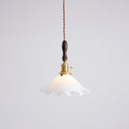 This Clérachic pendant light hangs against a pale grey wall, its white shade lit gently around the brass socket.