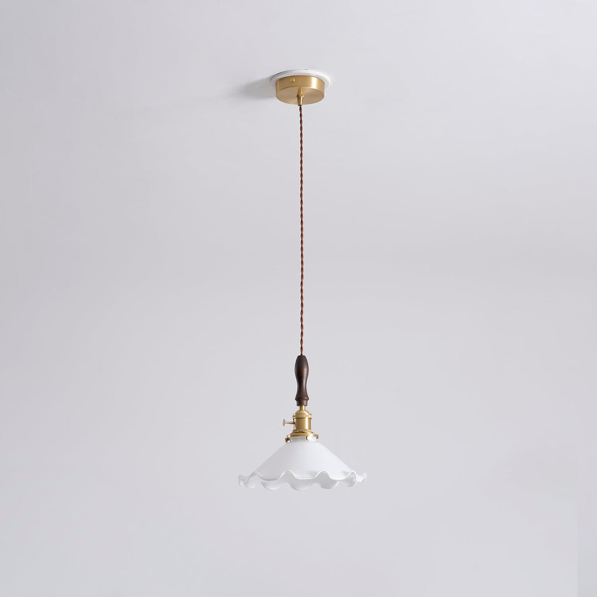 A Clérachic pendant light hangs from a round brass ceiling plate on a twisted cord, shown small against a pale ceiling.