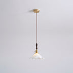 The same ceiling-plate view of this Clérachic pendant light, with the white shade lit and a twisted cord running down from the brass canopy.