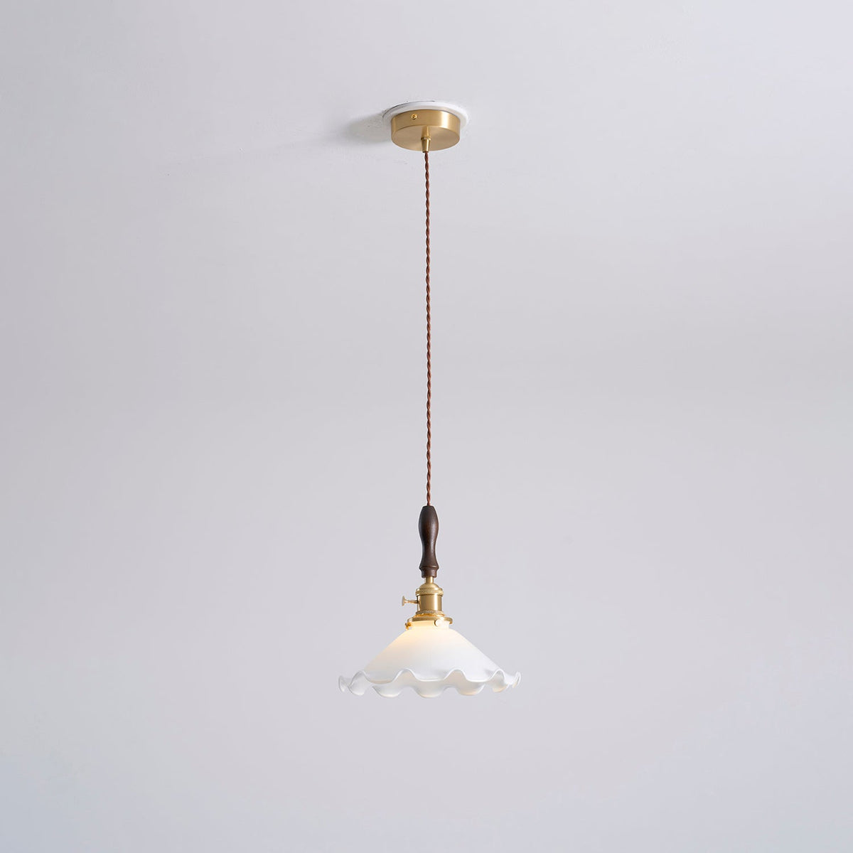 The same ceiling-plate view of this Clérachic pendant light, with the white shade lit and a twisted cord running down from the brass canopy.