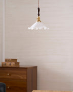 A small Clérachic pendant light hangs high on a textured cream wall above a walnut cabinet and a pair of books.