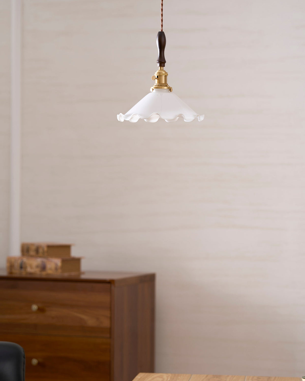 A small Clérachic pendant light hangs high on a textured cream wall above a walnut cabinet and a pair of books.