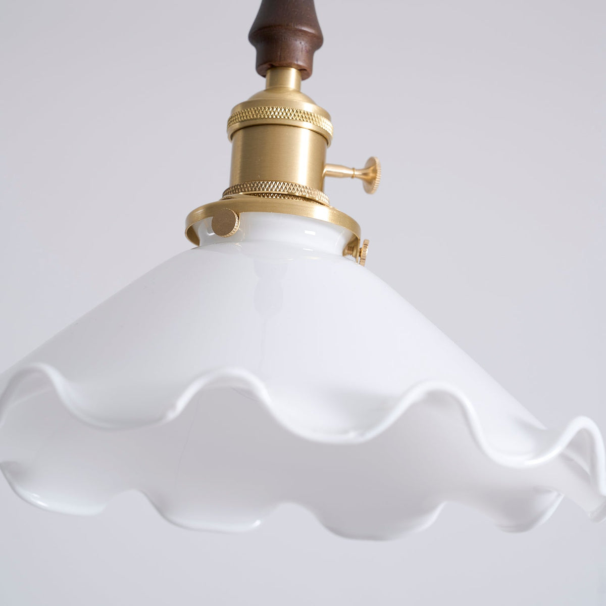 Close view of the wavy rim of the white glass shade and the brass socket on this Clérachic pendant light.