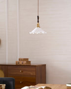 This Clérachic pendant light hangs on a textured wall above a walnut cabinet, with a dark chair at the bottom edge.