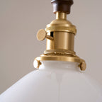 Close view of the knurled brass socket and turn switch on this Clérachic pendant light, above the white glass shade.