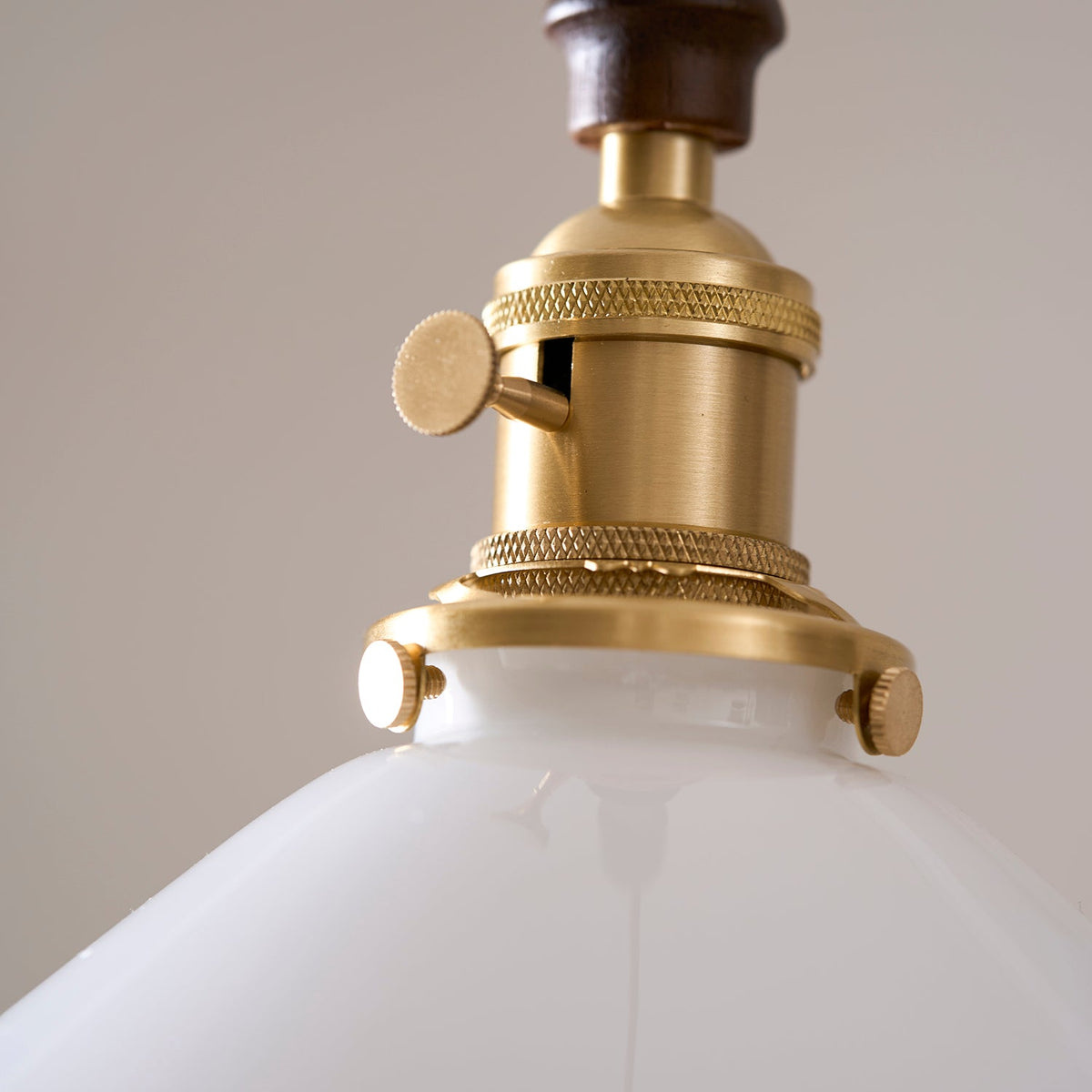 Close view of the knurled brass socket and turn switch on this Clérachic pendant light, above the white glass shade.