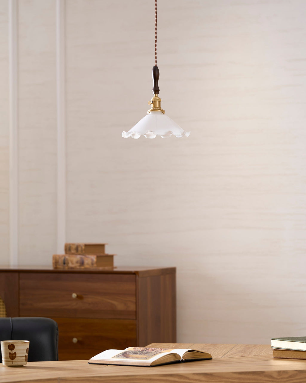 A Clérachic pendant light hangs on a cream wall above a walnut cabinet, an open book and a mug on a wooden desk.