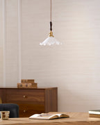 A Clérachic pendant light hangs on a cream wall above a walnut cabinet, an open book and a mug on a wooden desk.