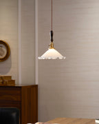 The white shade of this Clérachic pendant light lit warmly against a cream wall, with a round frame and walnut cabinet behind.