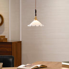 A Clérachic pendant light hangs close above a wooden desk, with an open book, green books and a walnut cabinet behind.