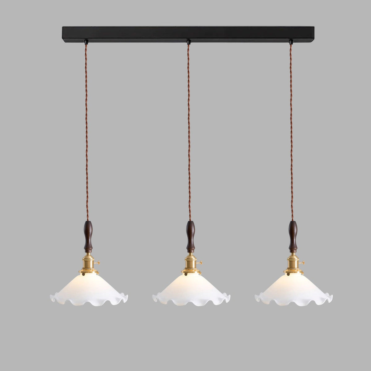 Three Clérachic pendant lights hang from a long black bar on twisted cords against a grey backdrop.