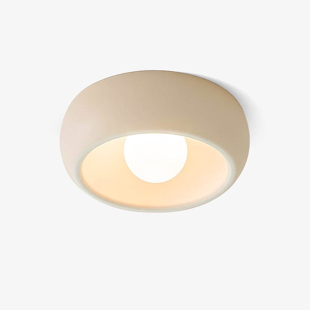 Beige Clérachic flush ceiling light on a plain white backdrop, a rounded shallow bowl with a round white bulb in its pale glowing interior.