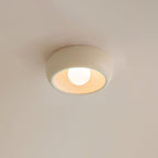 A beige Clérachic flush-mount light seen from below against a soft cream ceiling, its inside glowing warm.