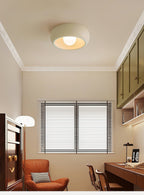 Beige Clérachic ceiling light in a small study with white mouldings, an orange armchair, a desk and green wall cabinets.