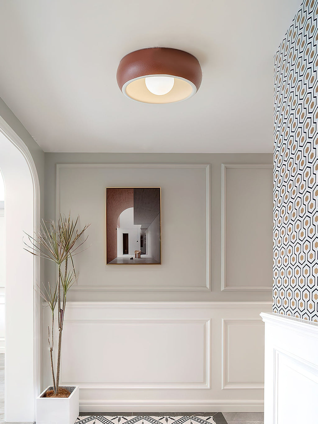 Wider view of a red Clérachic ceiling light in a panelled entrance, with a framed print and a plant in a white pot below.