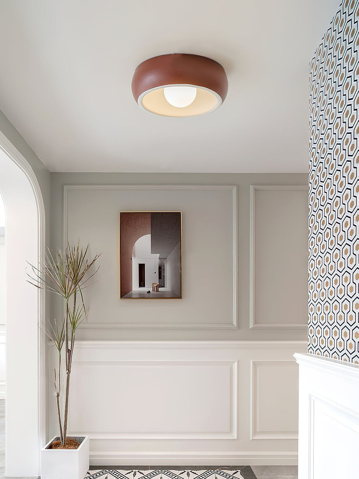 Wider view of a red Clérachic ceiling light in a panelled entrance, with a framed print and a plant in a white pot below.