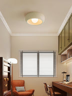 Beige Clérachic ceiling light centred in a study, with white cornicing, a rust-coloured armchair and a window with blinds below.
